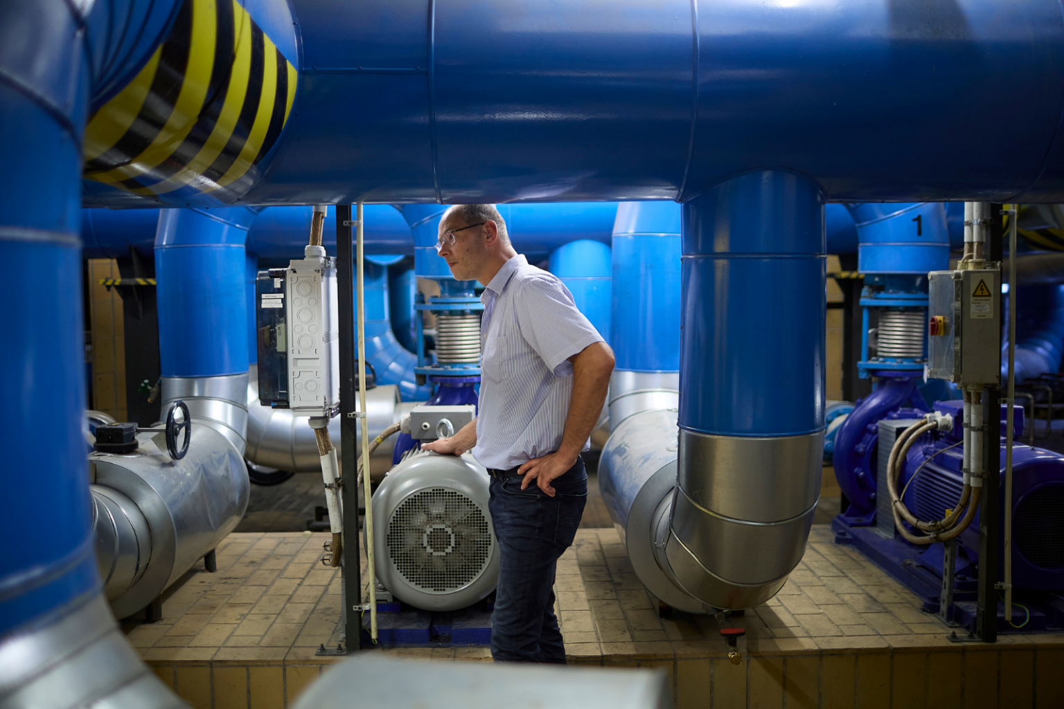 Fachkraft in der Technik arbeitet zwischen blauen Rohren in einem industriellen Raum