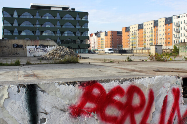 Berlin-Grafitti auf einer Mauer im Vordergrund, im Hintergrund ältere Hochhäuser in Berlin
