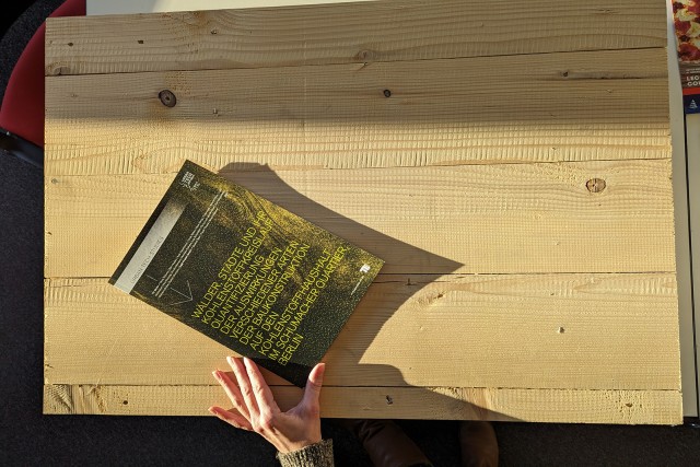 Eine Hand schiebt die gedruckte Publikation der Holzbaustudie präsentierend auf einen Holztisch.
