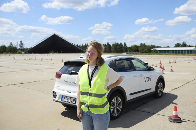 Person in Warnweste steht vor einem ferngesteuerten Fahrzeug auf einem Testgelände