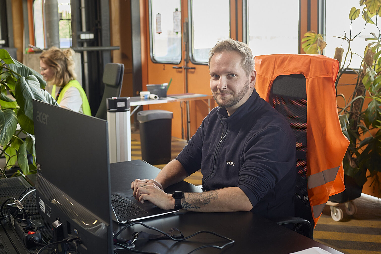 Person an einem Computerarbeitsplatz bei Vay mit Testfahrzeug im Hintergrund