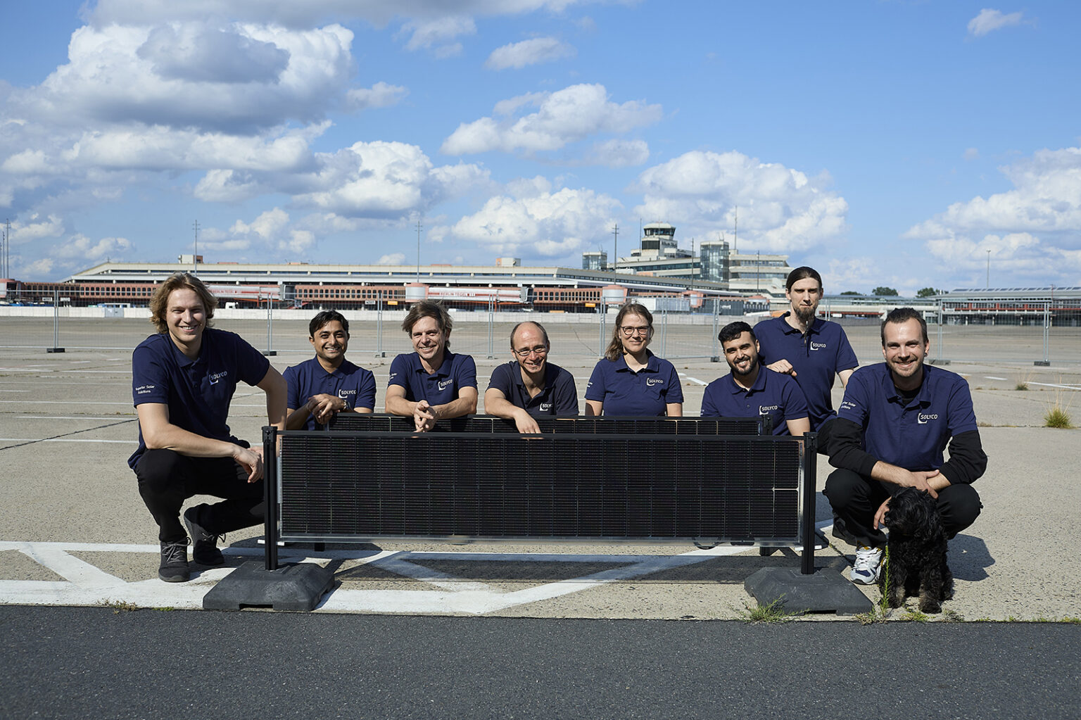 Gruppe von acht Personen posiert vor einer Solaranlage auf dem Flughafengelände Tegel